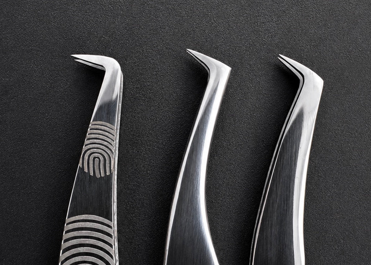 Three metallic precision tweezers with curved tips arranged vertically on a dark textured background. The left tweezers feature an engraved fingerprint pattern on the handle.